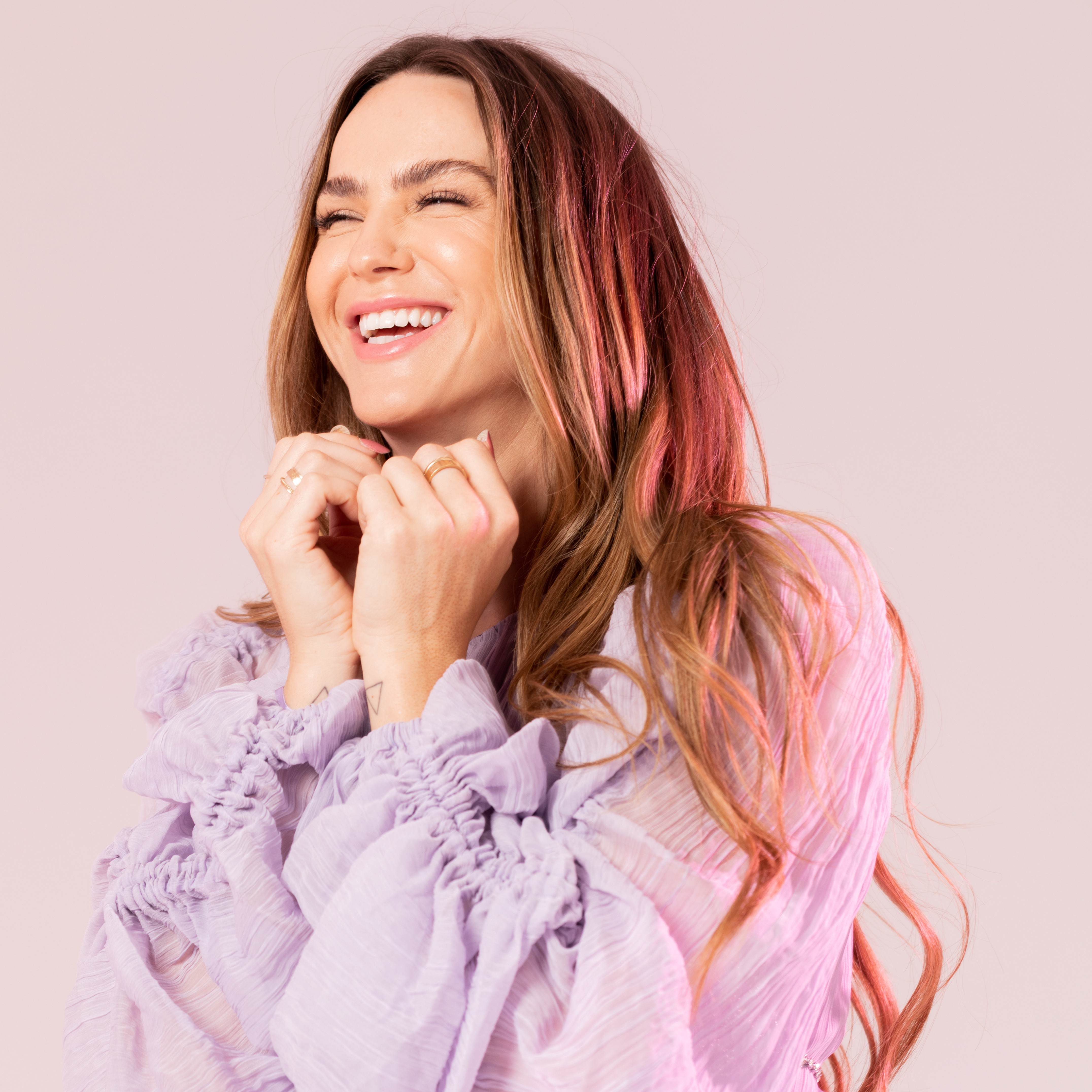 Photo: A woman smiling and looking left of camera with her hands posed under her chin.