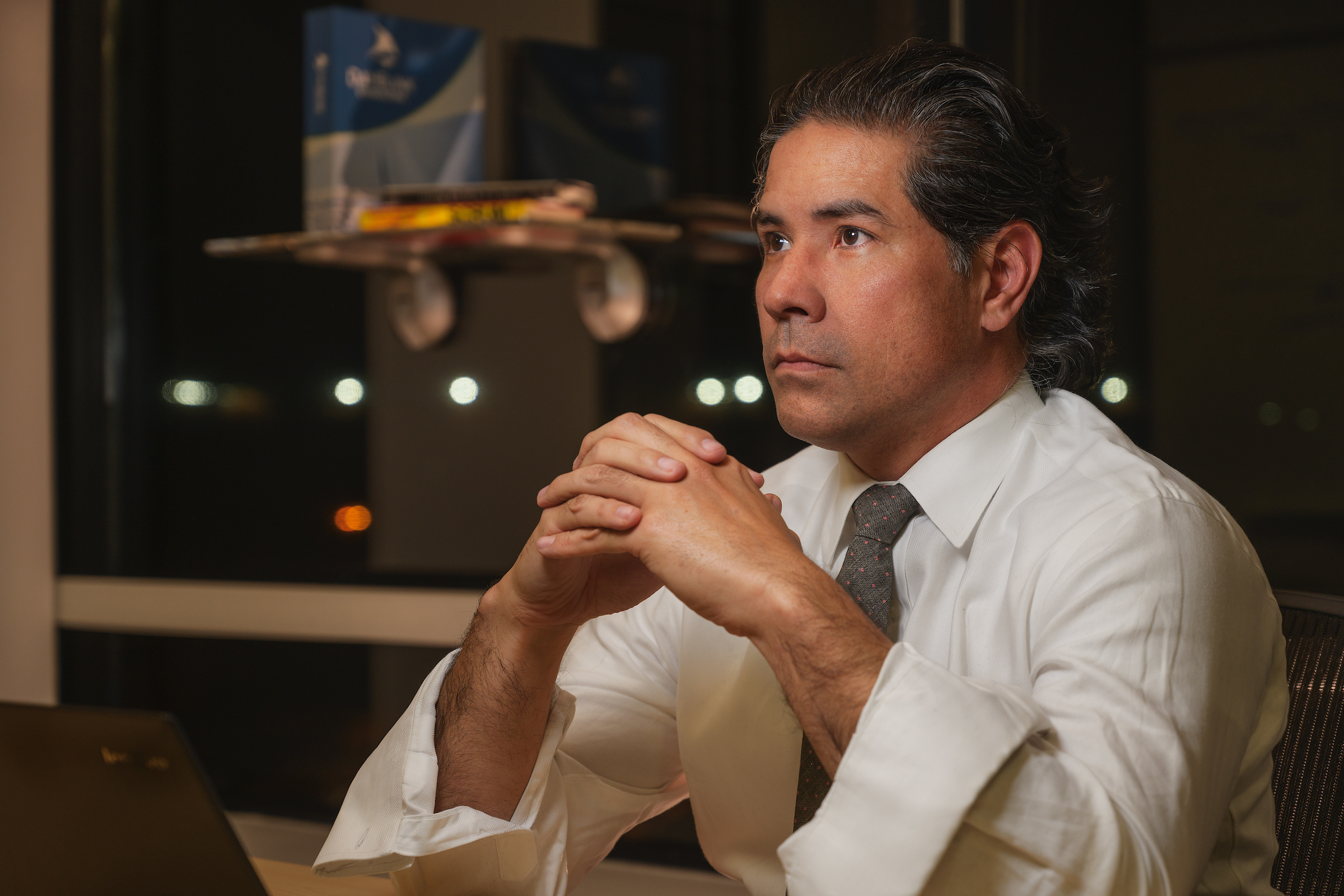 PHOTO: Male, sitting with his elbows on the table, fingers interlaced, looking off into the distance.